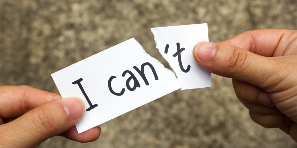 Woman' hand holding a card with text can't over cement background. Tear "'t" for change concept to positive concept. Concept and idea background.